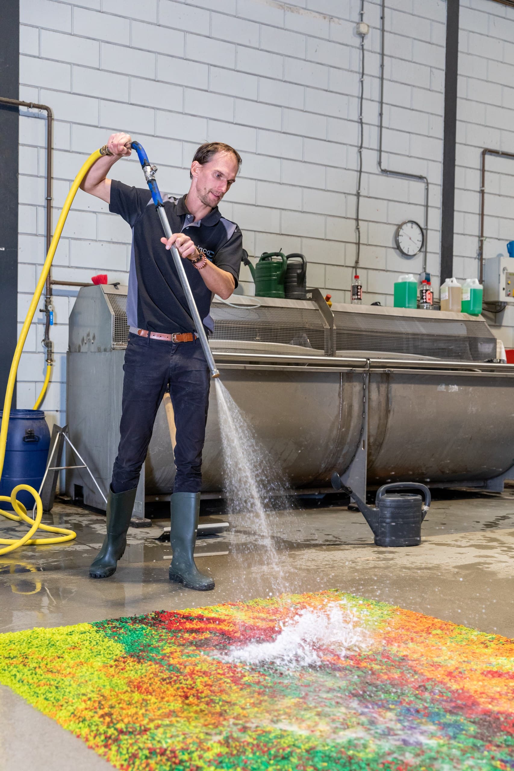 Medewerker spoelt een kleurrijk hoogpolig vloerkleed met water in de wasserij