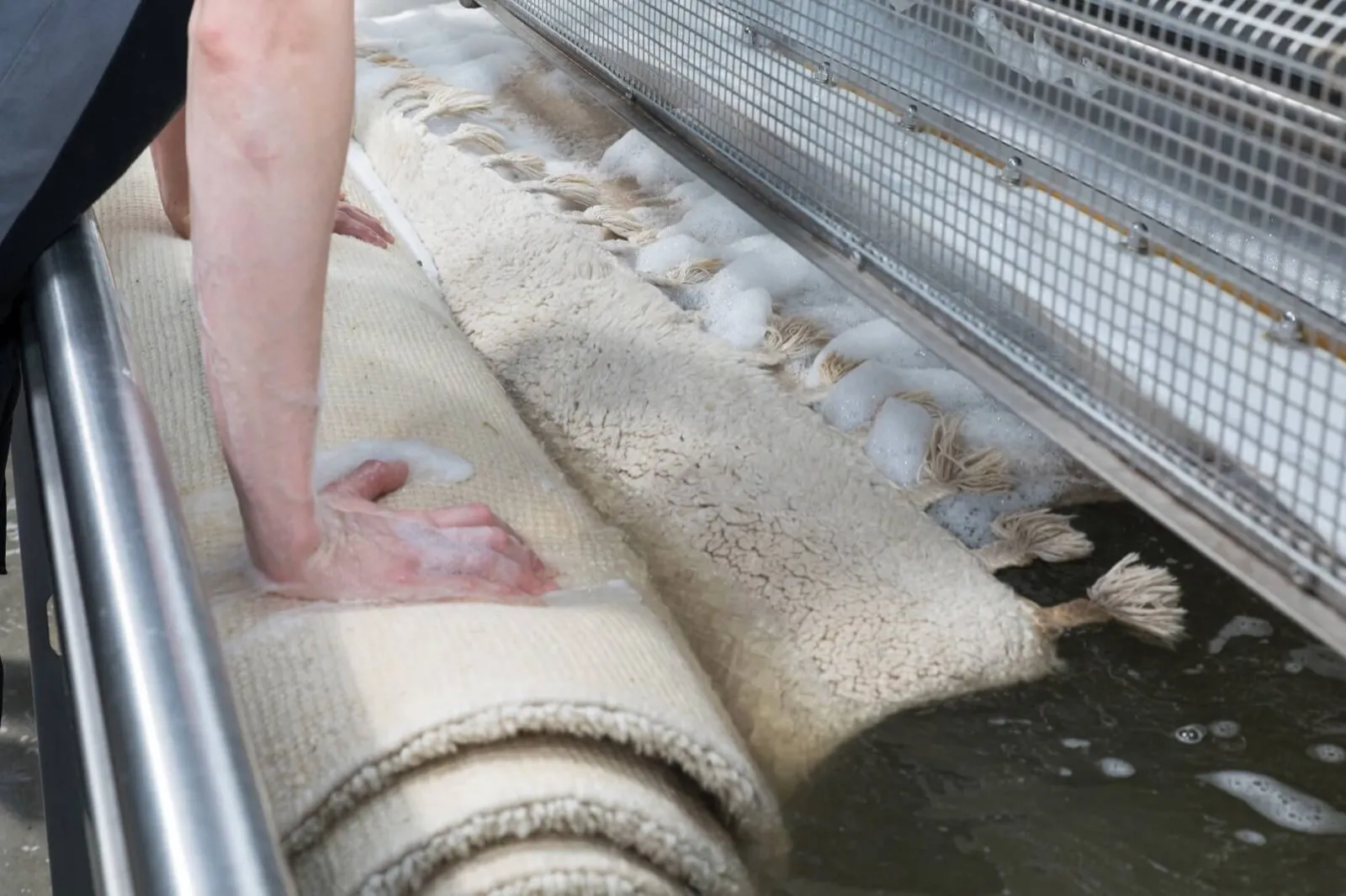Medewerker wast een crème wollen kleed met franjes met de hand in de spoelbak