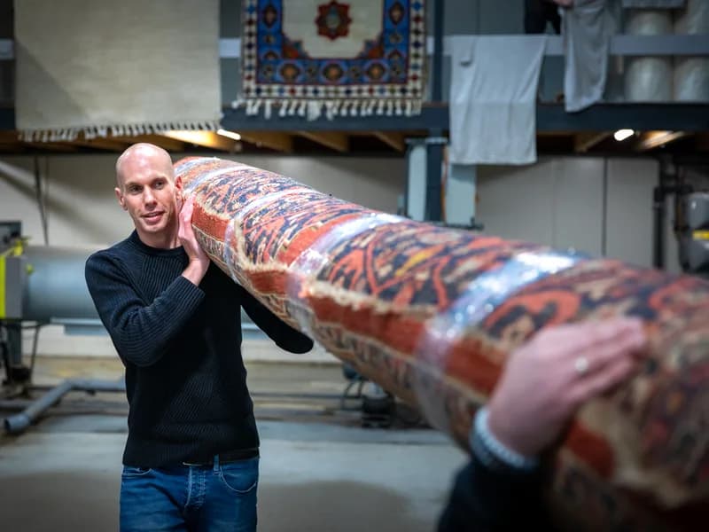 Kleda medewerker draagt vloerkleed in de wasserij — ophaalservice door heel Nederland