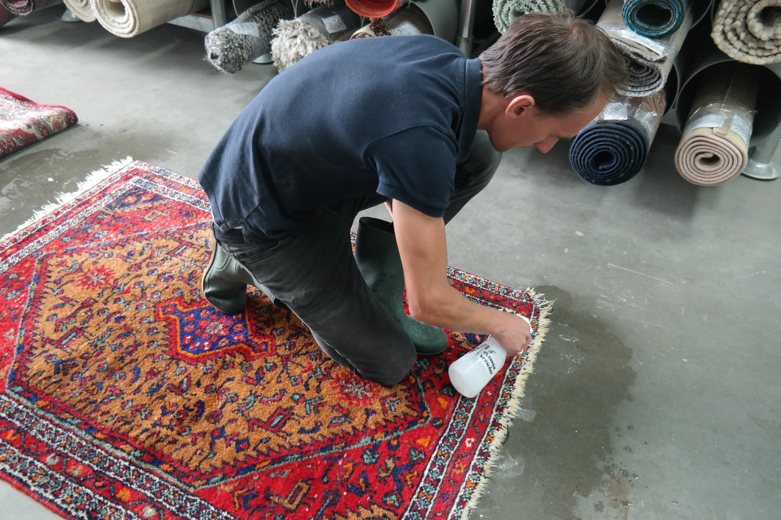 Medewerker behandelt de franjes van een rood Perzisch vloerkleed met een sprayflacon