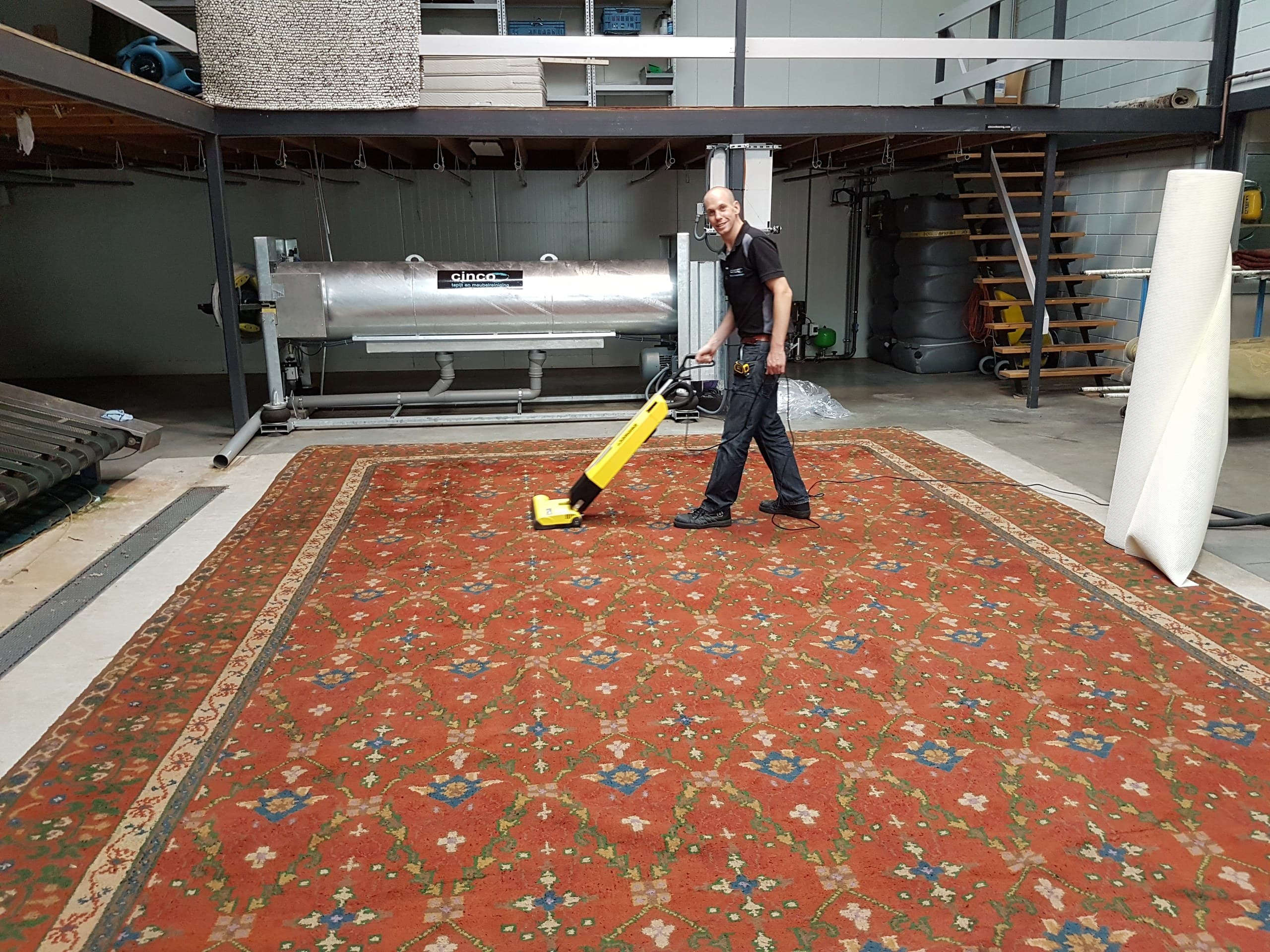Medewerker borstelt een groot vloerkleed na in de wasserij