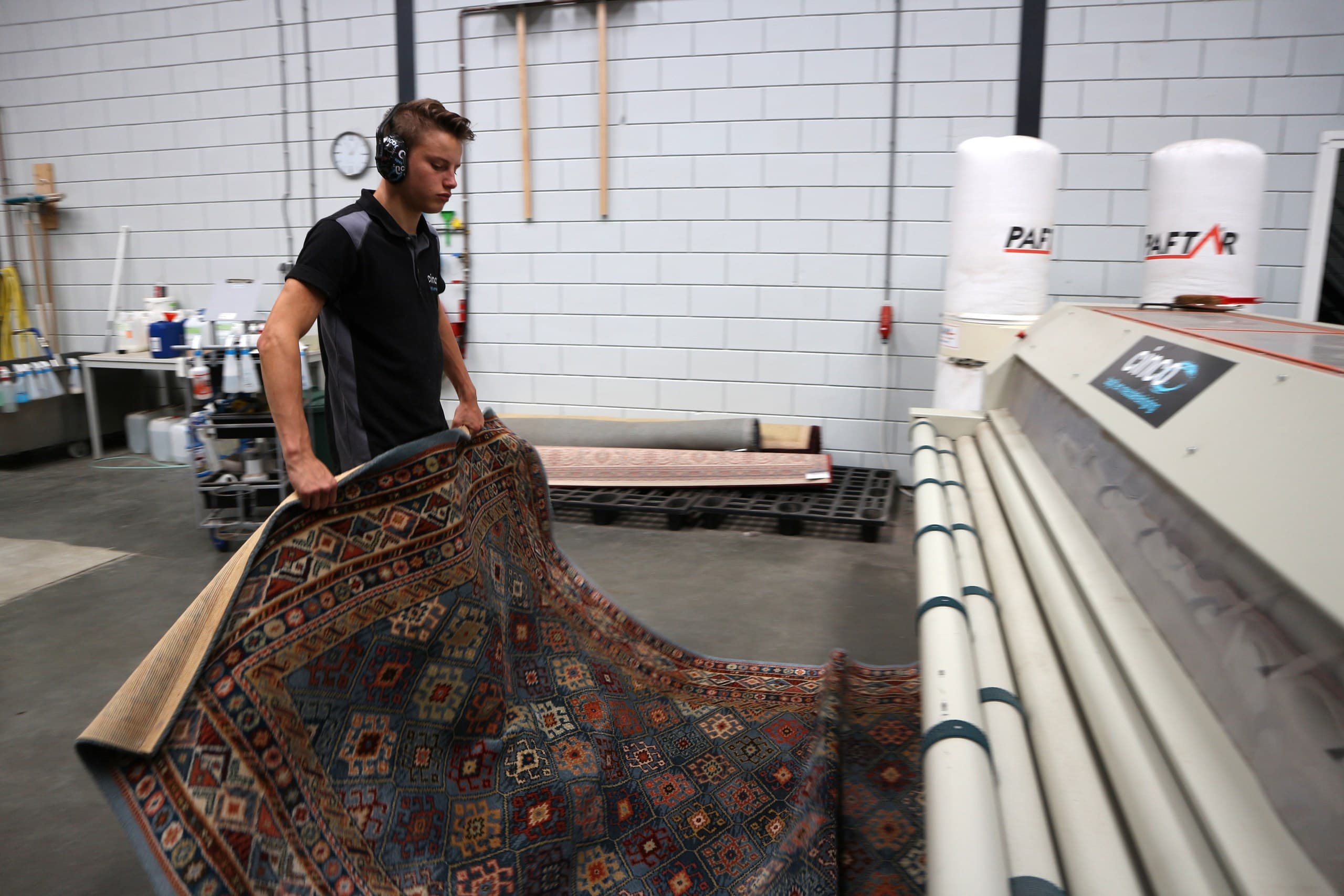 Medewerker tilt handgeknoopt vloerkleed op in de reinigingshal van de wasserij
