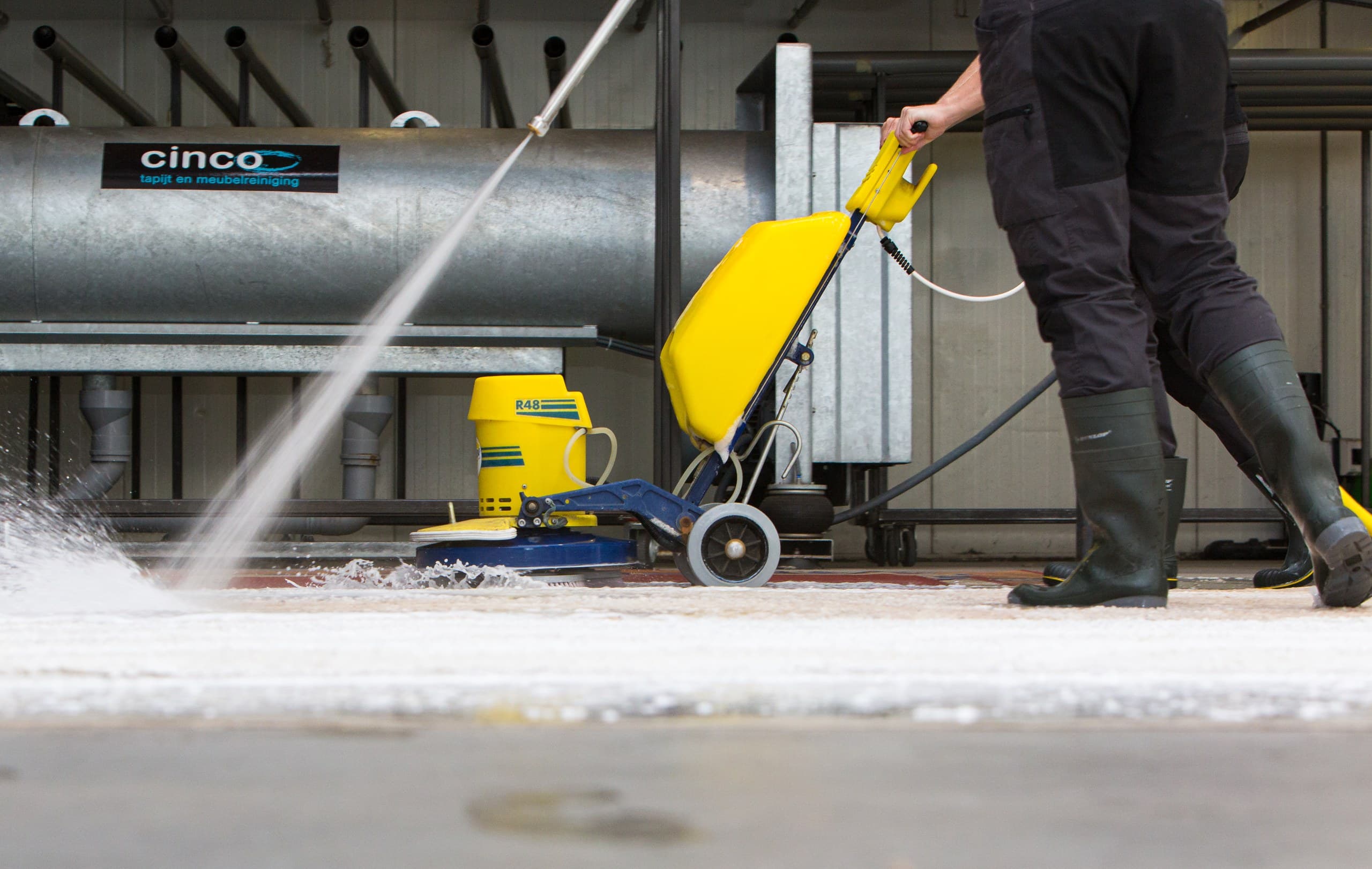 Medewerker reinigt een vloerkleed met de schrobmachine in de wasstraat